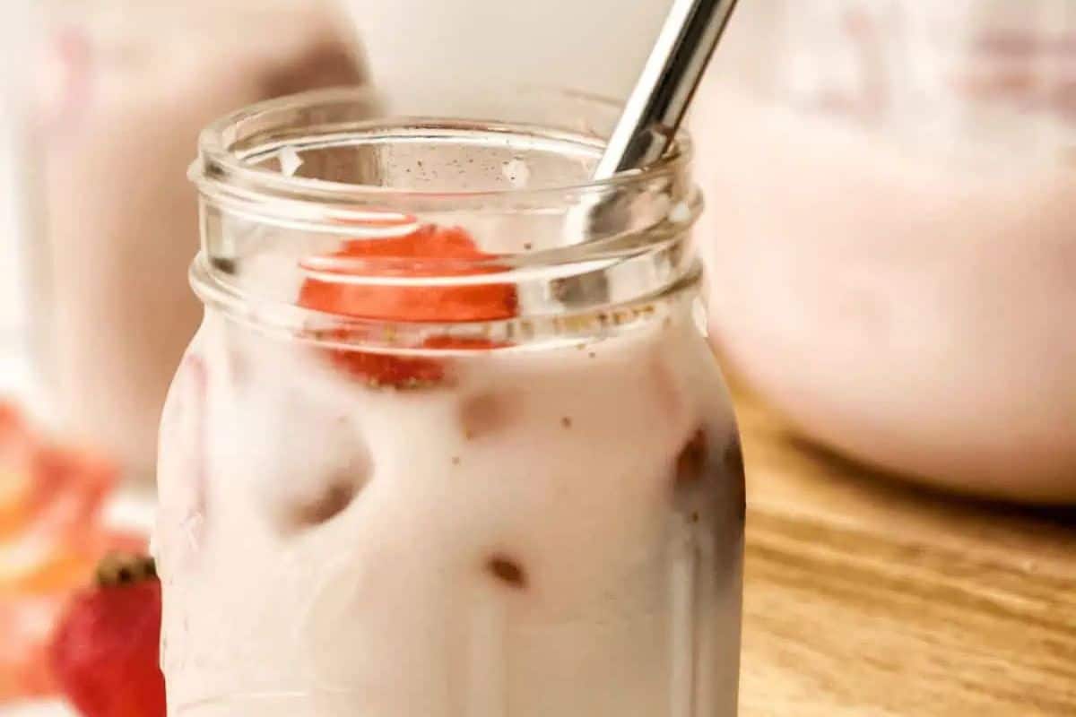 Close-up of a glass of strawberry horchata, garnished with a strawberry and a metal straw.
