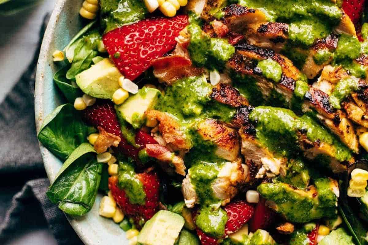 A mouthwatering salad with grilled chicken, fresh spinach, sliced strawberries, avocado, corn, and green dressing in a bowl—perfect for those who love summer salads.