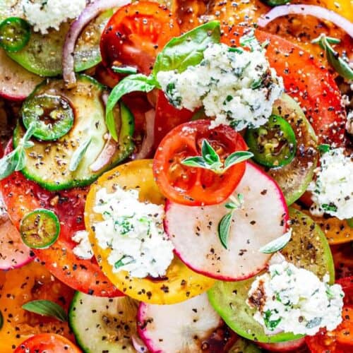 A colorful summer salad with sliced tomatoes, cucumbers, radishes, red onions, fresh basil leaves, ricotta cheese, and cracked black pepper—perfect for lovers of mouthwatering salads.