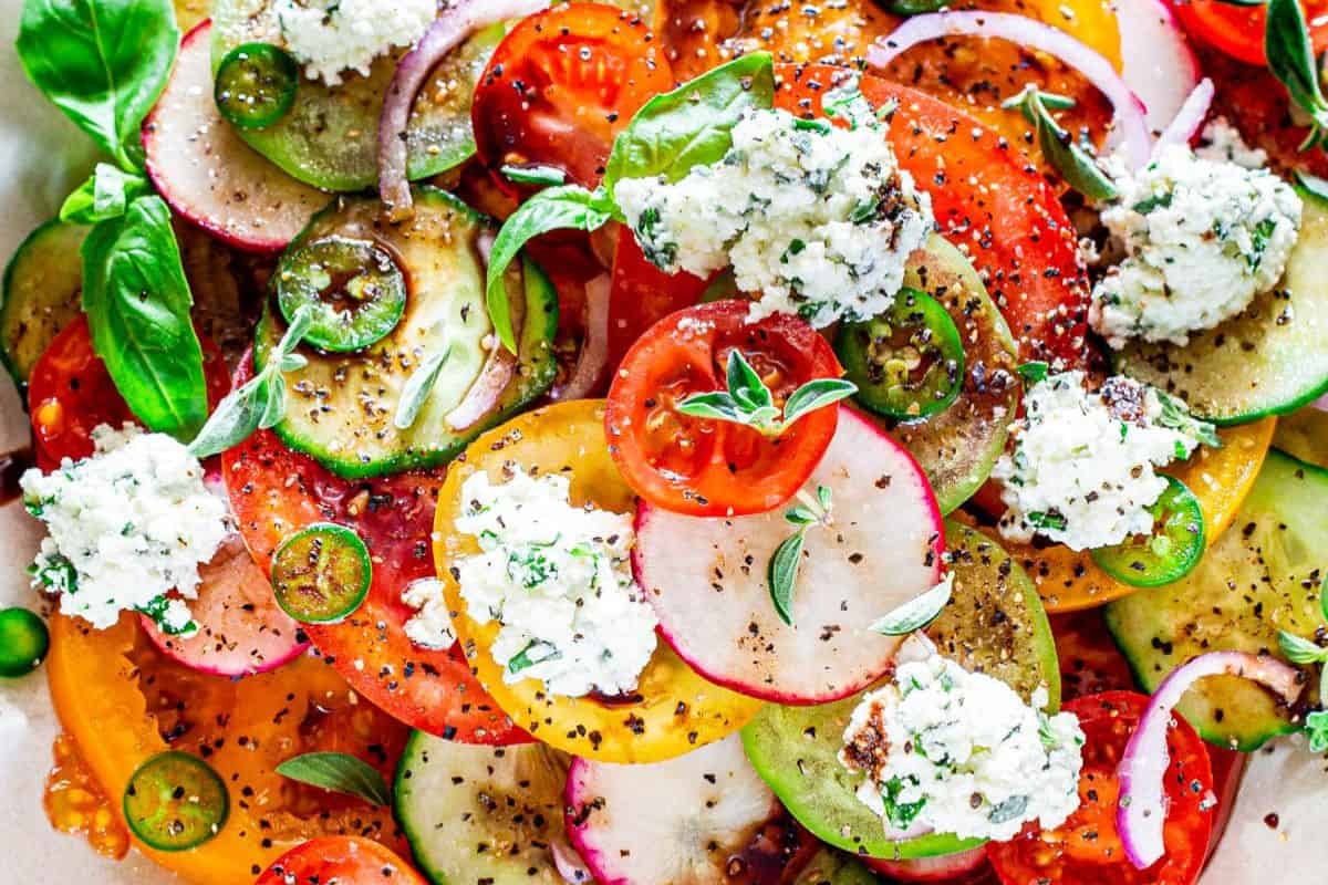 A colorful summer salad with sliced tomatoes, cucumbers, radishes, red onions, fresh basil leaves, ricotta cheese, and cracked black pepper—perfect for lovers of mouthwatering salads.