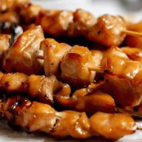Several skewers of grilled, glazed chicken pieces are arranged closely together on a white surface, perfect for trying out new kabob recipes.