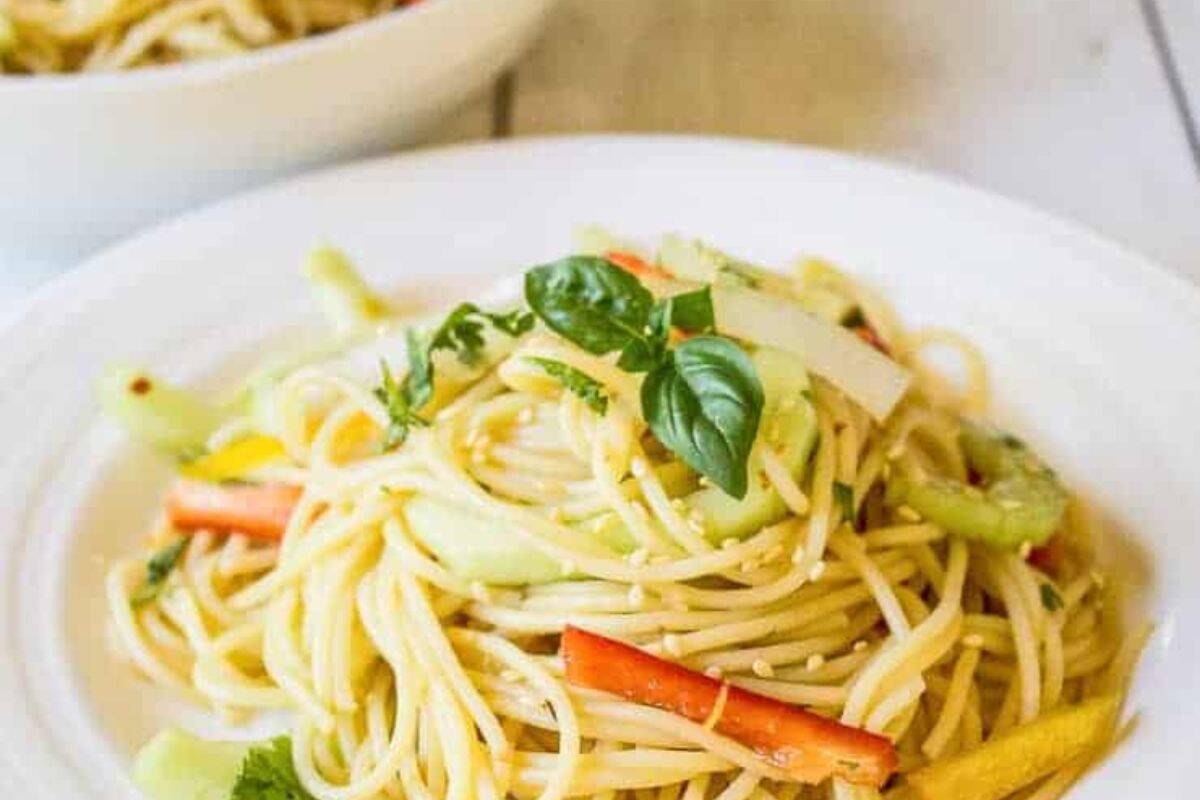 A plate of spaghetti topped with sliced vegetables, sesame seeds, and fresh basil, this dish is perfect for summer salads and seasonal recipes, served on a white dish.