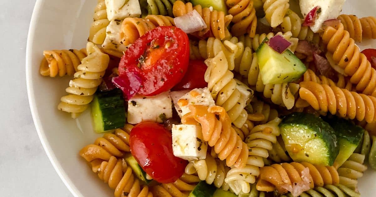 A delicious bowl of tender tossed with cherry tomatoes, cucumber, red onion, and cubes of cheese, all perfectly seasoned with fresh herbs.