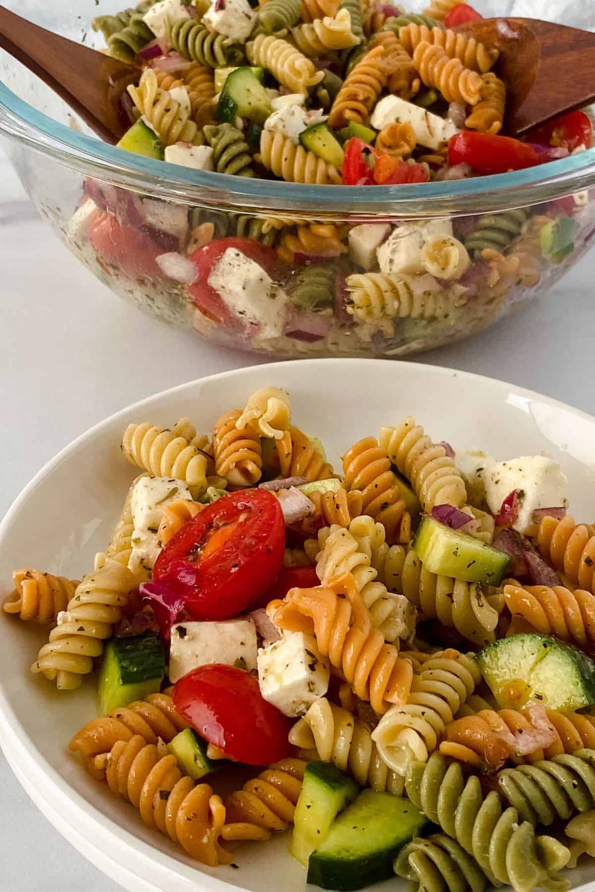 A colorful bowl and plate  with cherry tomatoes, cucumber, red onion, feta cheese, and fresh herbs, beautifully served on a crisp white surface.