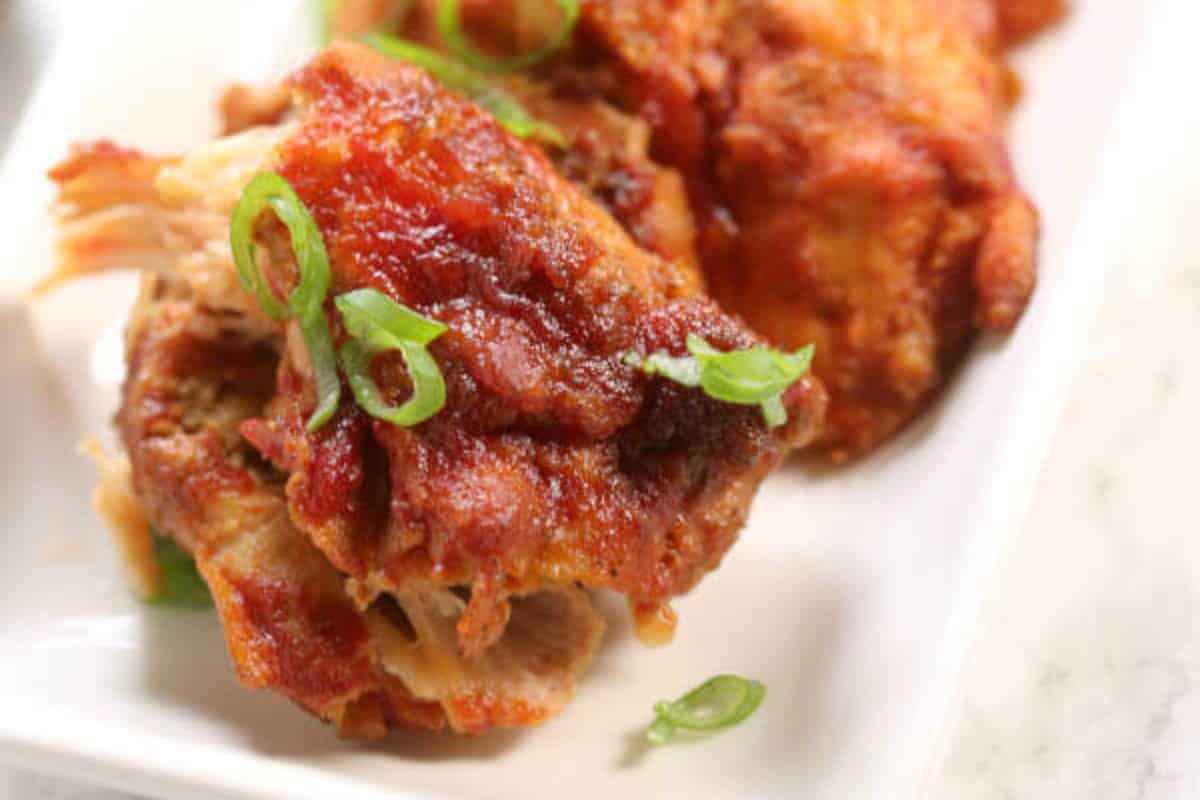 A very close up picture of a chicken thigh that is covered with brown sauce and topped with green onions. In the background there is a blurred version of another chicken thigh. 