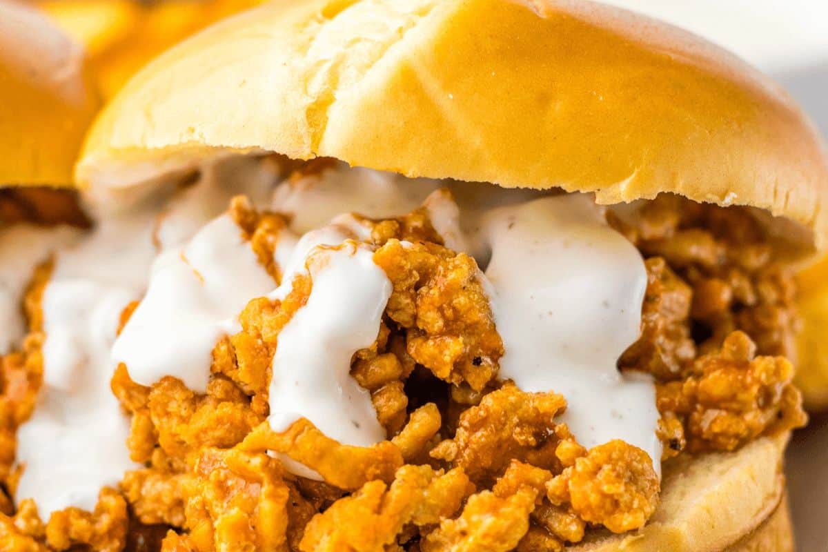 A close up of the top and bottom of a burger bun stuffed with ground chicken topped with ranch dressing. 