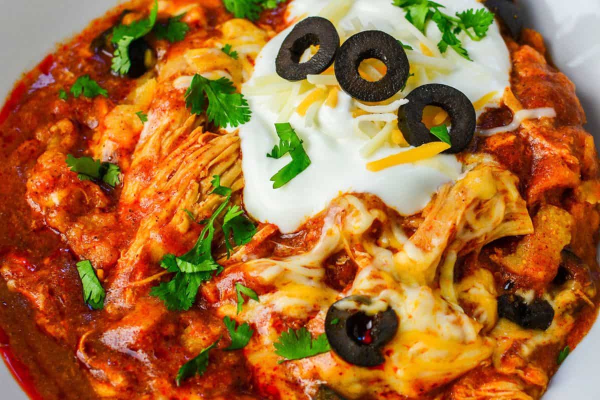 White bowl of chicken enchilada crockpot casserole with sour cream on top. 