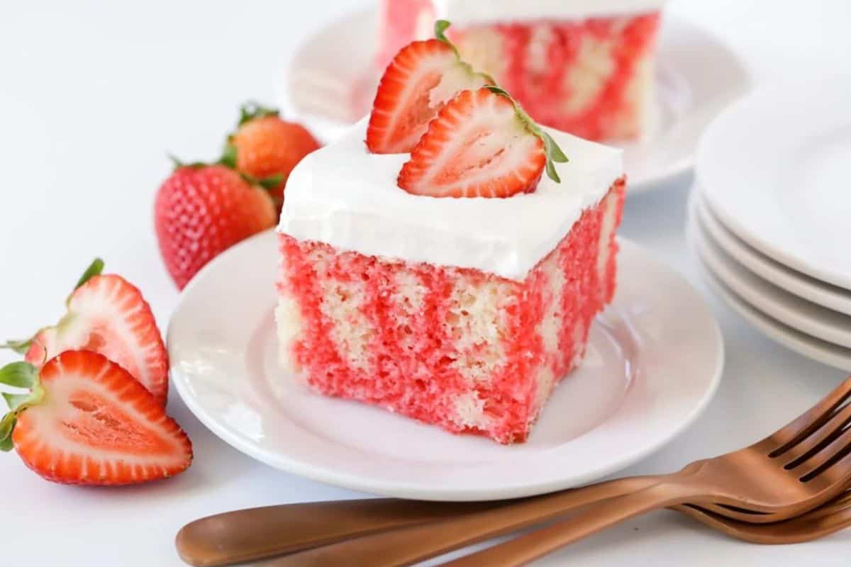 Piece of jello poke cake on plate with fresh strawberries. 