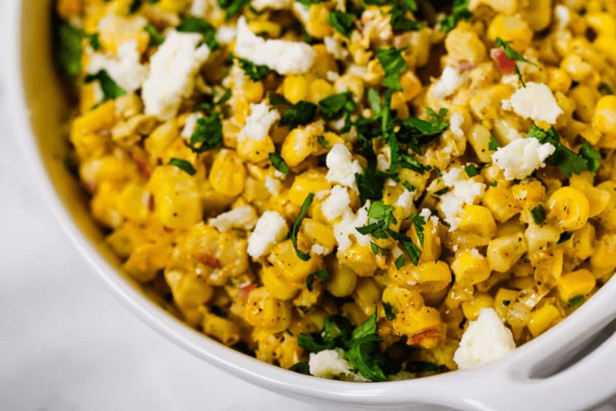 In a white ceramic dish, corn is mixed with red onions, chili powder, cilantro and topped with crumbles of queso fresco.  