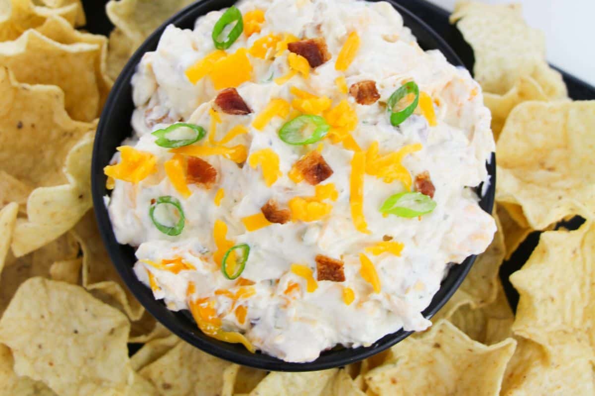 A bowl of bacon ranch cheddar dip surrounded by chips. 