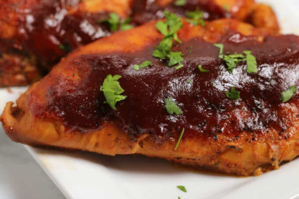 A close up of two chicken breasts covered in barbeque sauce and topped with parsley. 
