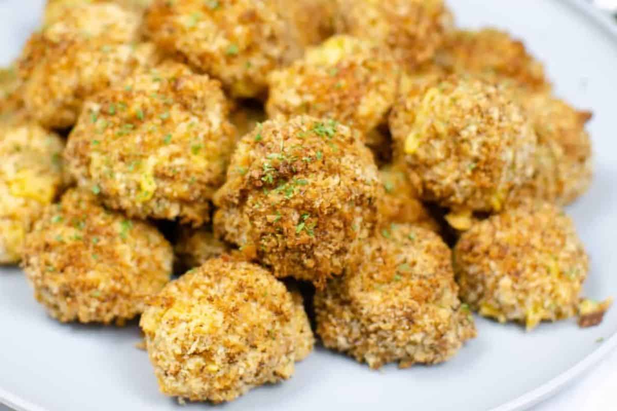 On a white plate, breadcrumb balls are browned and topped with green herbs. On a few of the balls you can just see a yellow, cheese color where the cheese has oozed out of the breadcrumb coated ball.  
