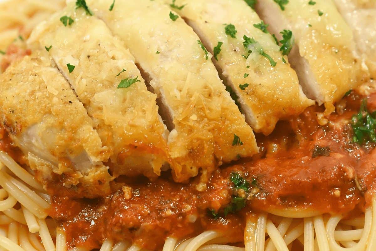 A close up of spaghetti topped with a red sauce, parmesan crusted chicken slices and parsley. 