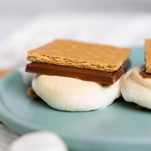 An Air Fryer S'mores treat made with a toasted marshmallow, a piece of chocolate, and a graham cracker sits on a blue plate.