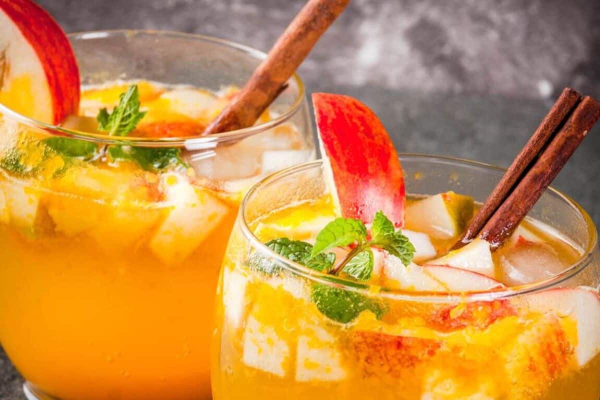 Two glasses of golden apple cider mojitos garnished with apple slices, mint, and cinnamon sticks.