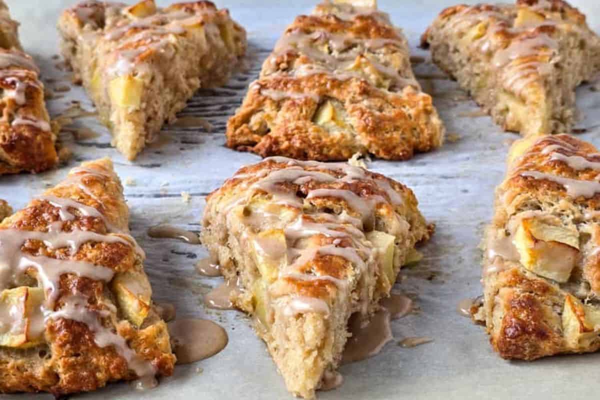 Golden-brown apple scones with a drizzle of maple cinnamon glaze are arranged on parchment paper.