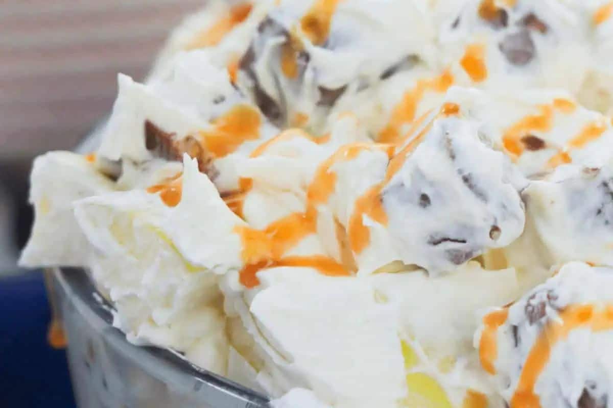 Close-up of a creamy dessert in a bowl topped with apple pieces, chocolate, and caramel drizzle.