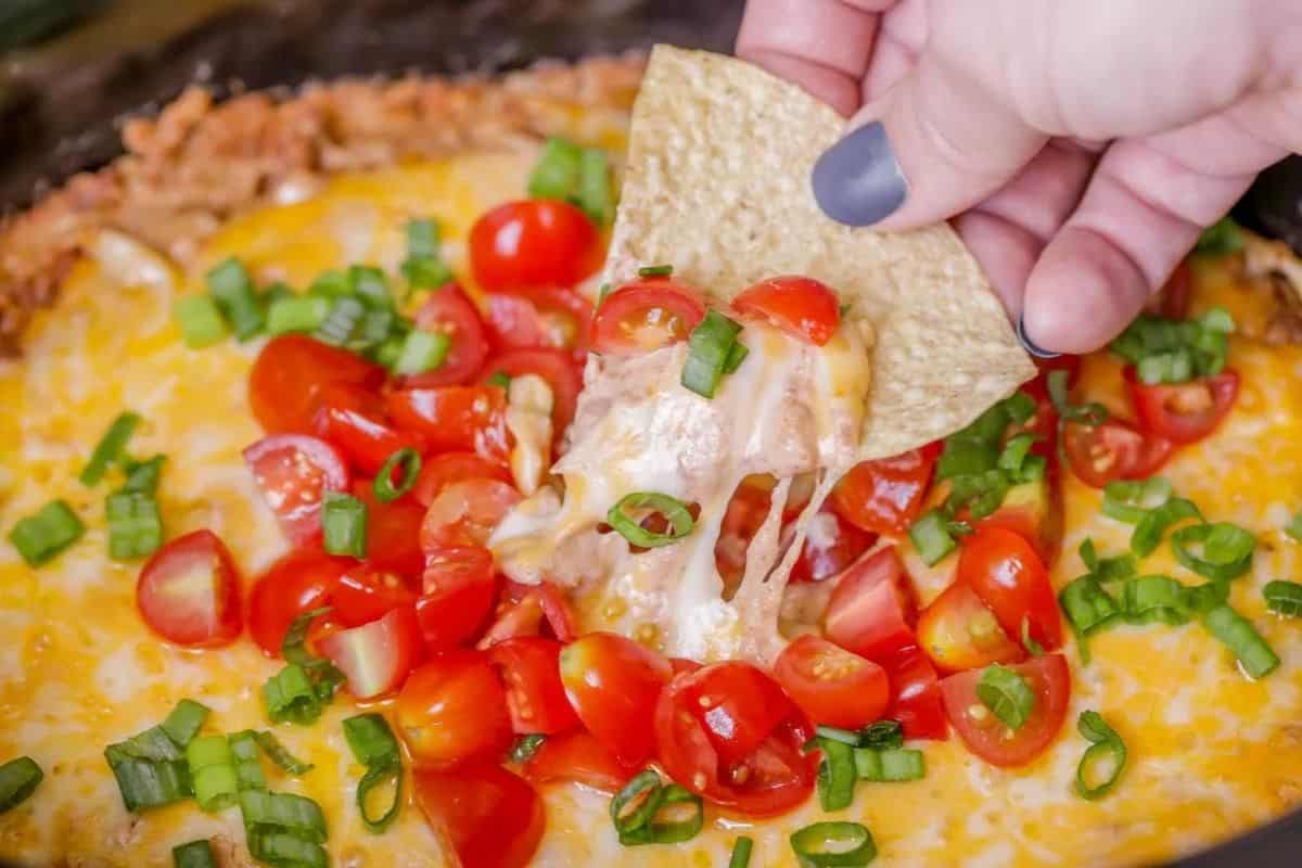 A hand holding a tortilla chip being dipped into a bowl of bean dip.