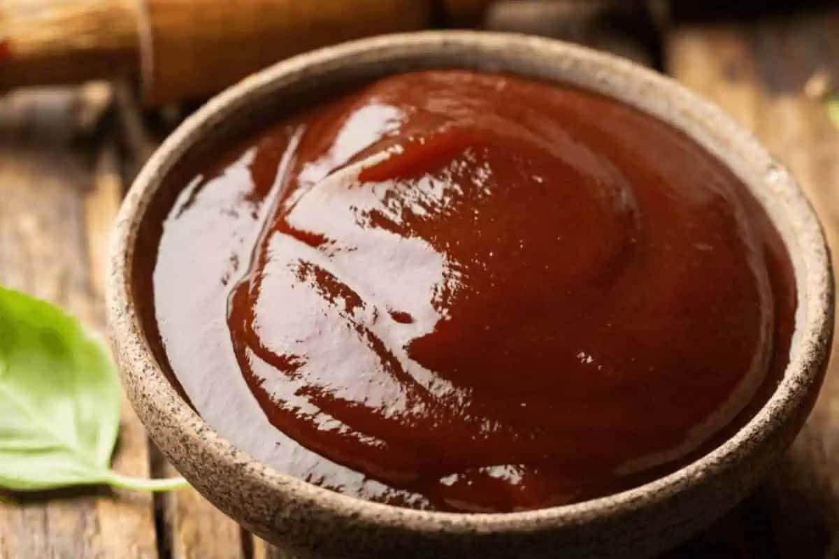 A ceramic bowl filled with thick, dark brown homemade BBQ sauce sits on a wooden surface.