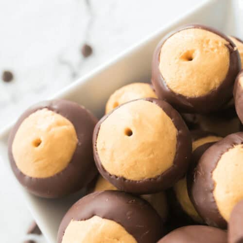 A bowl of buckeye candy, featuring creamy peanut butter centers partially dipped in chocolate, sits on a marble surface.