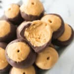 A bowl filled with buckeye candy, showcasing chocolate-dipped peanut butter balls, one with a bite taken, displayed on a white marble surface.