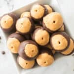 A square bowl filled with candies, a delightful treat featuring a layer of peanut butter partially dipped in chocolate, rests elegantly on a white marble surface.