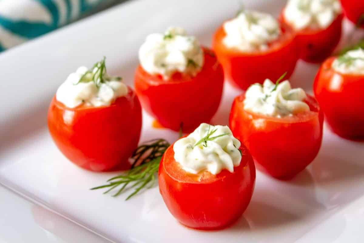 A plate of hollowed cherry tomatoes filled with a creamy white mixture and garnished with small sprigs of dill—a delightful addition to your fresh tomato recipes.