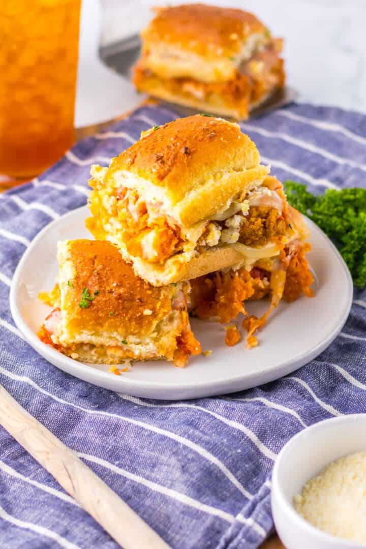 Two stacked Chicken Parm Sliders with fried chicken, tomato sauce, and cheese on a white plate, placed on a blue striped cloth.