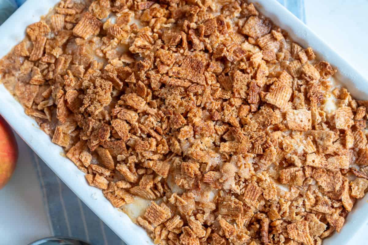 A rectangular baking dish filled with a golden-brown apple bake topped with crushed Cinnamon Toast Crunch.