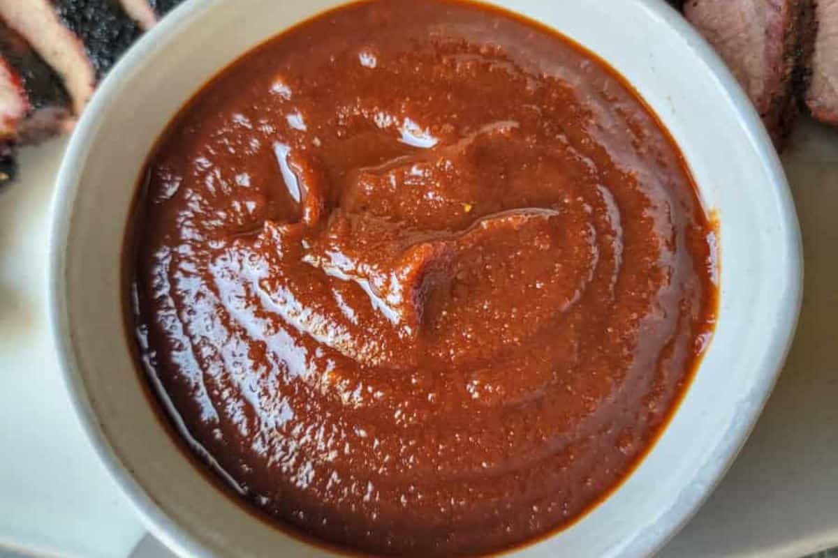 A close-up view of a bowl filled with thick, reddish-brown homemade BBQ sauce, perfect for trying out new BBQ recipes.