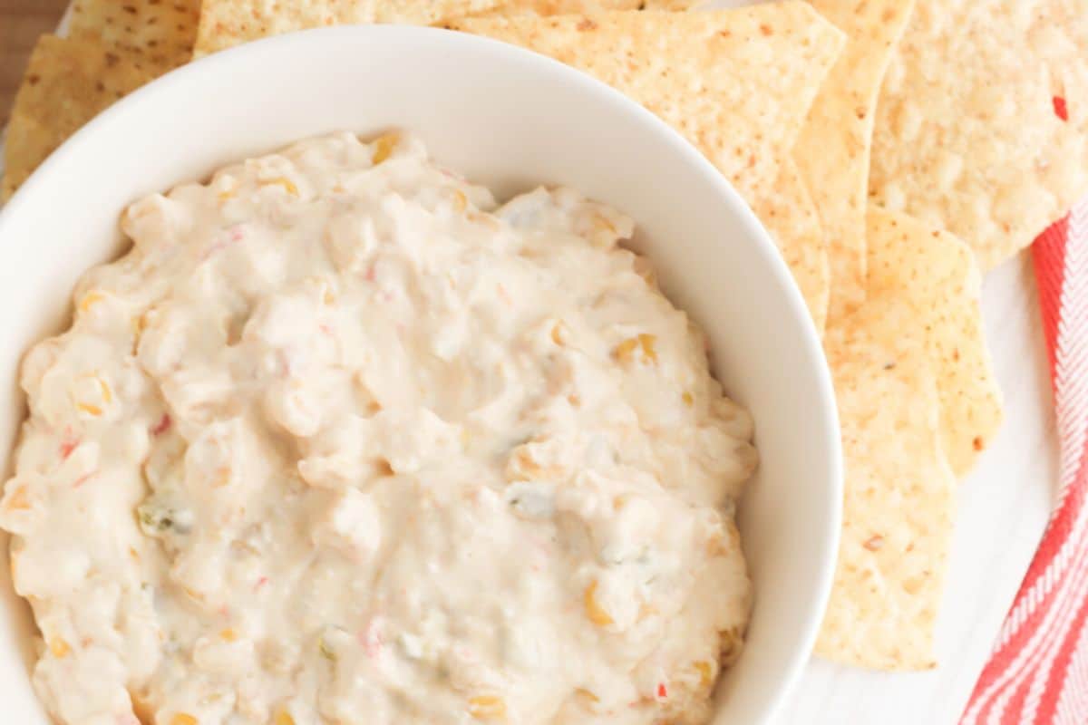 A bowl of cream cheese corn dip next to some tortilla chips. 