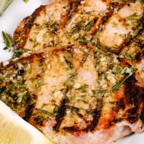 Grilled Boneless Pork Chops with herbs and visible grill marks, served with a lemon wedge on a white plate.