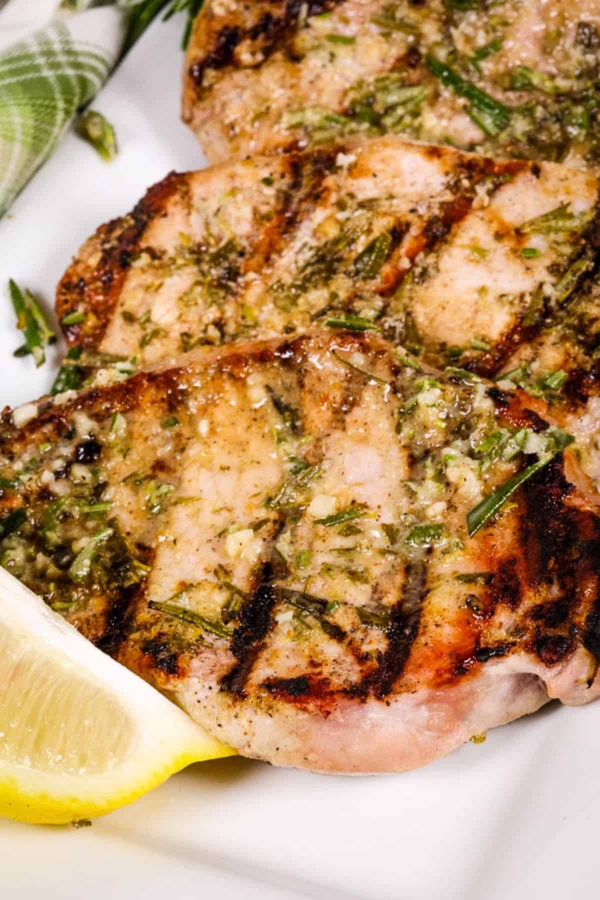 Grilled Boneless Pork Chops with herbs and visible grill marks, served with a lemon wedge on a white plate.