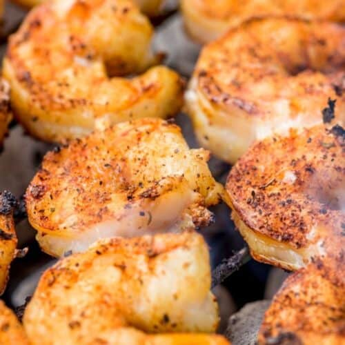 Close-up of shrimp skewers cooking on a grill, seasoned to perfection with visible grill marks and some smoke rising.