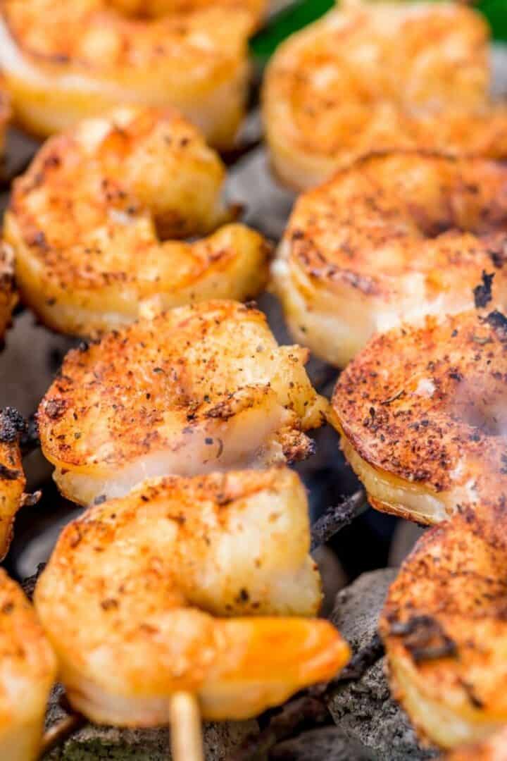 Close-up of shrimp skewers cooking on a grill, seasoned to perfection with visible grill marks and some smoke rising.