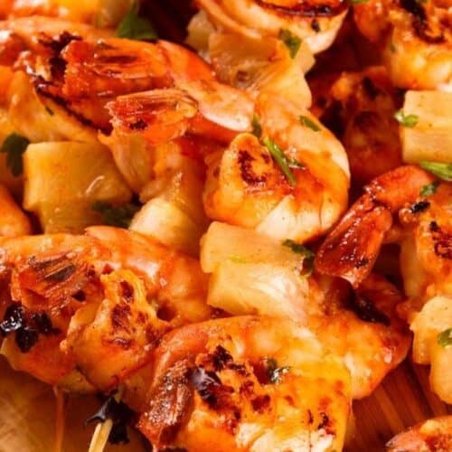 Grilled shrimp skewers and pineapple skewers rest on a wooden platter, garnished with fresh parsley and a lemon wedge.