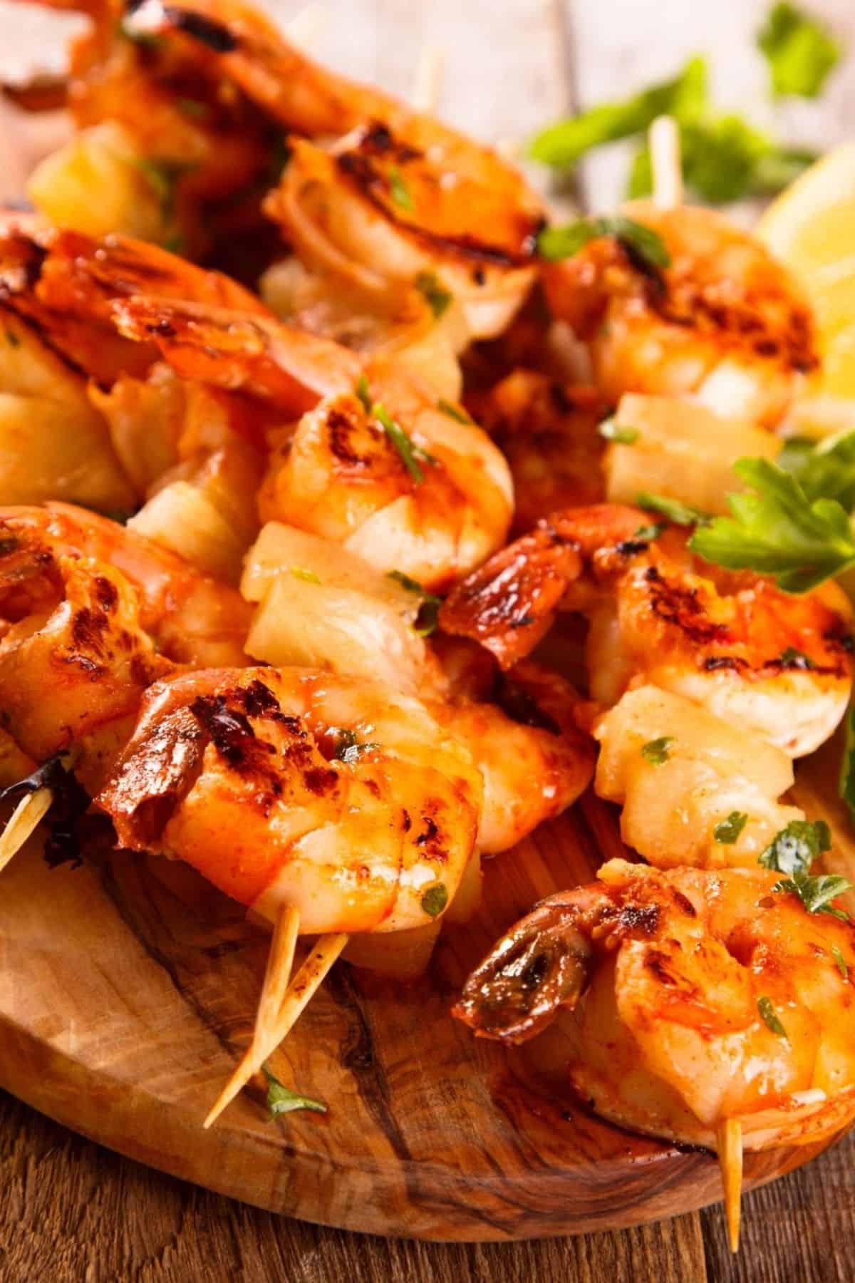 Grilled shrimp skewers with fresh herbs and lemon wedges are elegantly served on a wooden platter.