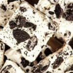 Squares of dessert bars topped with white frosting and crumbled chocolate cookies, reminiscent of an Oreo Ice Cream Cake, are arranged on a wooden surface.
