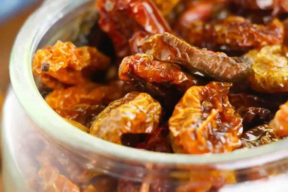 Close-up of a glass jar filled with dried red and orange chili peppers, perfect for adding bold flavor to seasonal recipes or spicy tomato recipes.