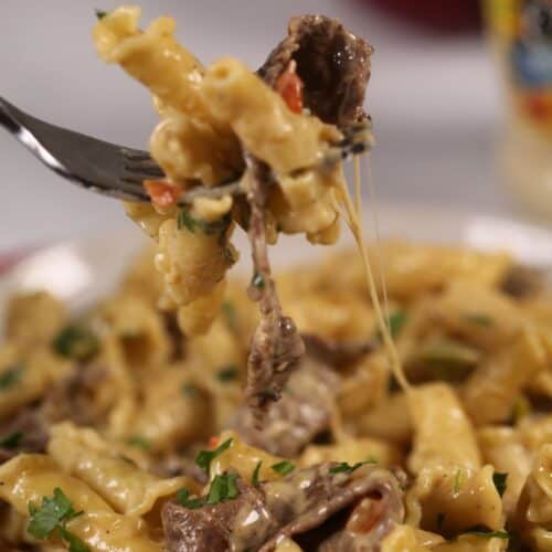A fork of the pasta under a plate of the philly cheese steak pasta.