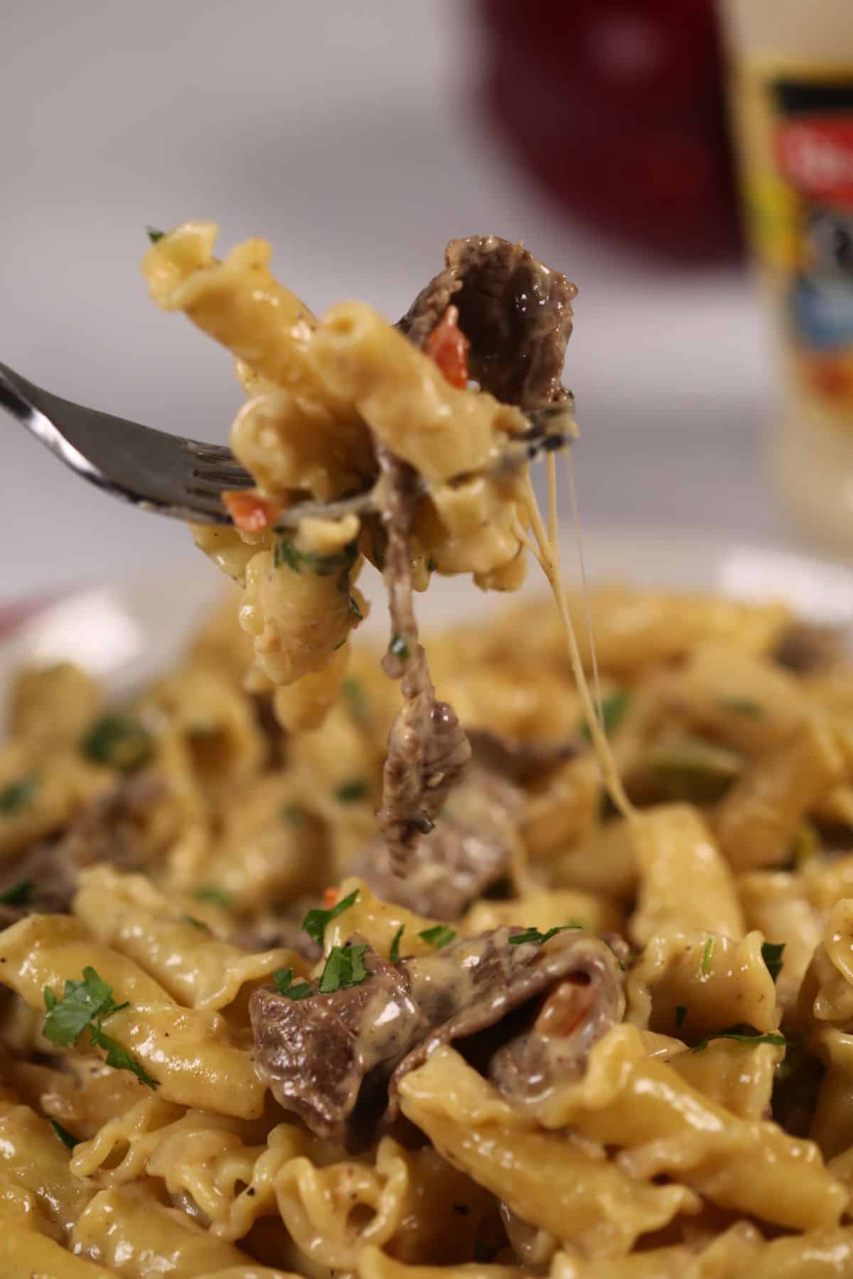 A fork of the pasta under a plate of the philly cheese steak pasta.
