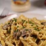 A finished dish of the ziti and meat with a jar of alfredo sauce in the back.