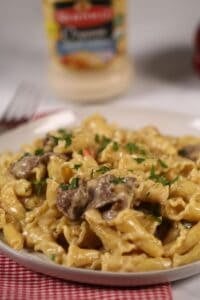 A finished dish of the ziti and meat with a jar of alfredo sauce in the back.