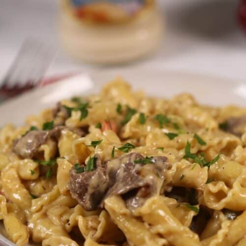 A finished dish of the ziti and meat with a jar of alfredo sauce in the back.
