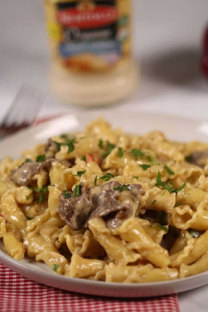 A finished dish of the ziti and meat with a jar of alfredo sauce in the back.