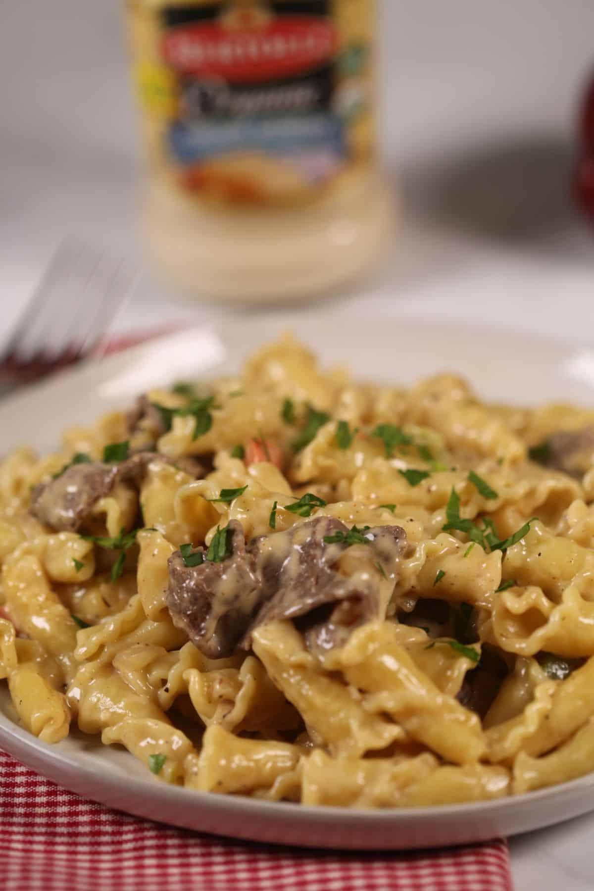 A finished dish of the ziti and meat with a jar of alfredo sauce in the back.