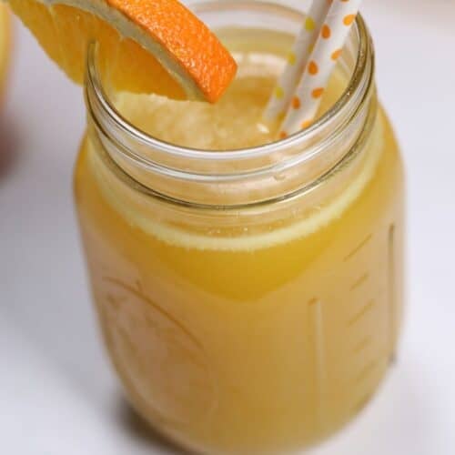 Mason jar of pineapple moonshine with an orange slice garnish and two patterned paper straws.