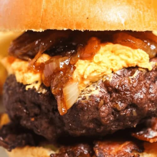 A pub burger on a bun topped with cheese, caramelized onions, and bacon.