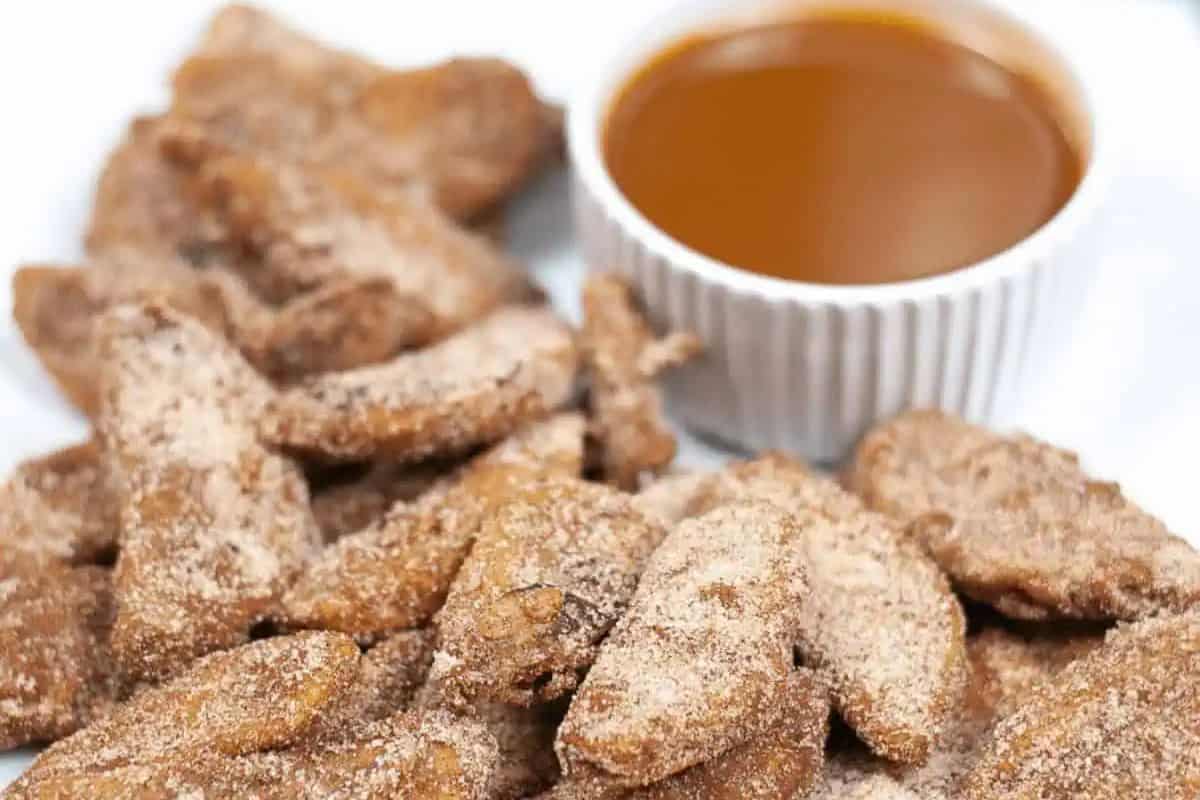 Cinnamon sugar-coated air-fried apple slices served with a small dish of caramel dipping sauce on a white plate.