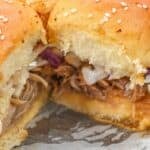 Close-up of pork sliders with coleslaw on sesame buns, featuring tender shredded pork, placed on a white surface.